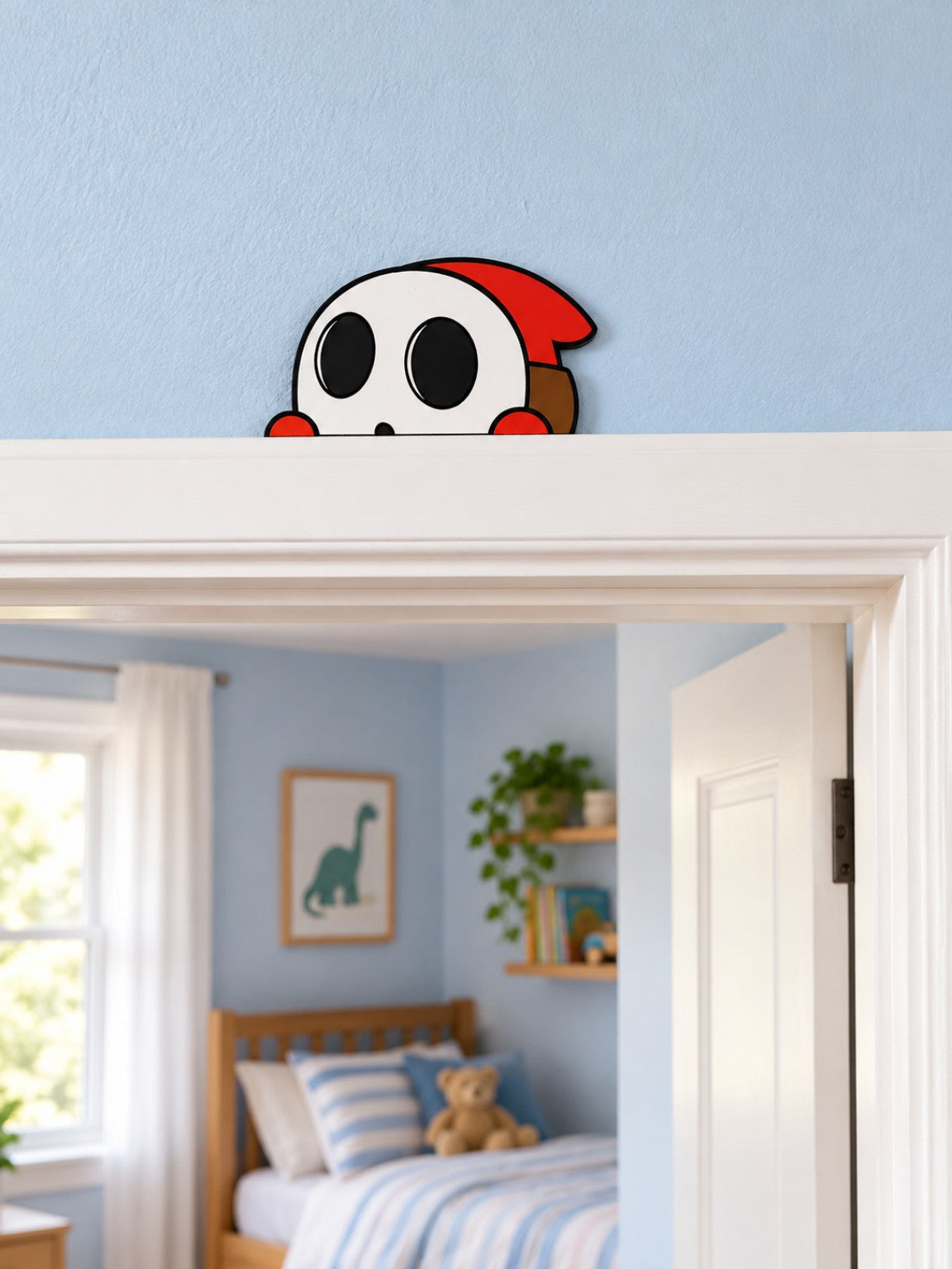 Red hooded 3D printed door peeper with white face and black eyes peeking over a white bedroom door frame